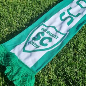 Grün-weißer SCO-Sommer-Fanschal mit Vereinswappen und Fransen auf einer Rasenfläche.
